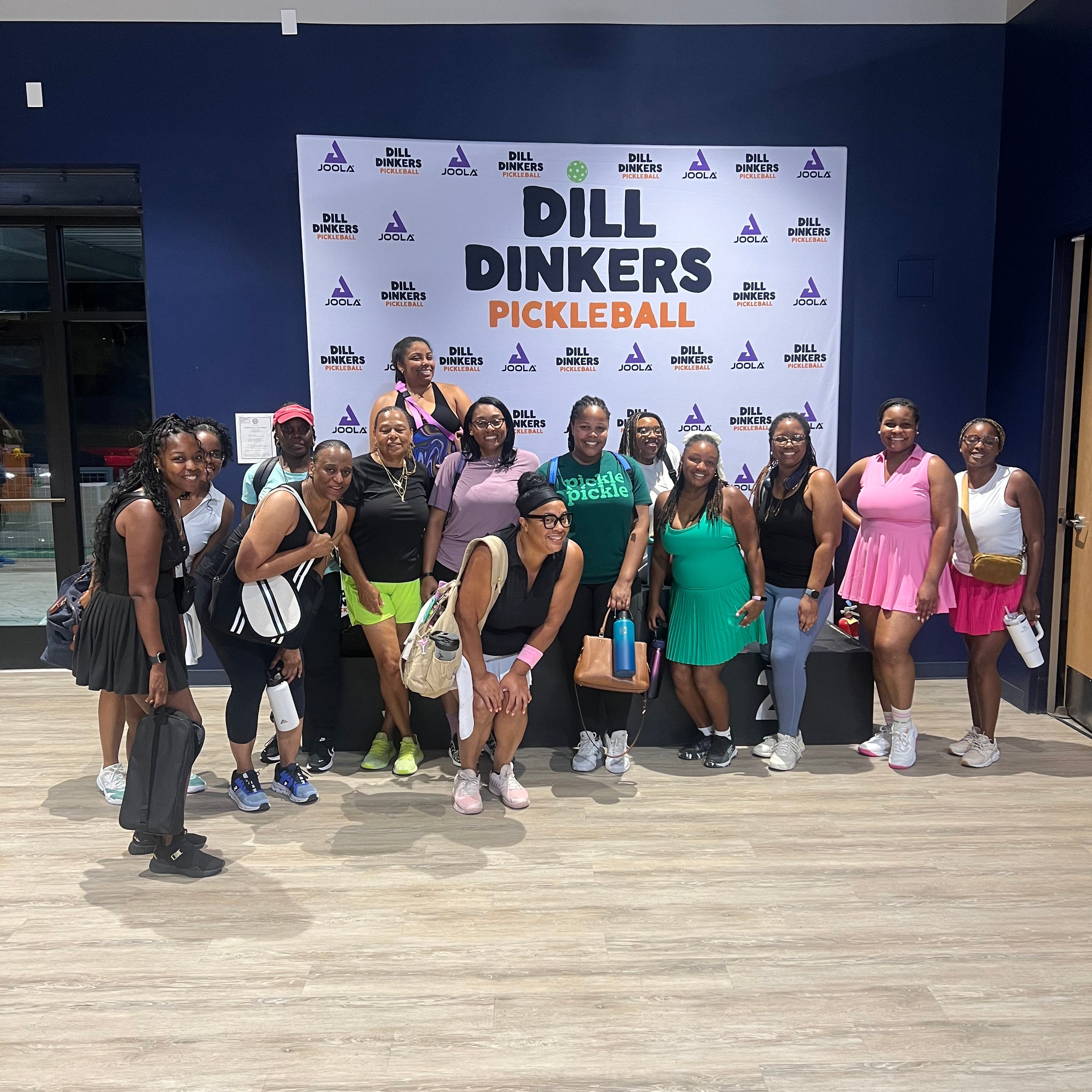 Group of people posing in front of a Dill Picklers Pickleball branded backdrop.